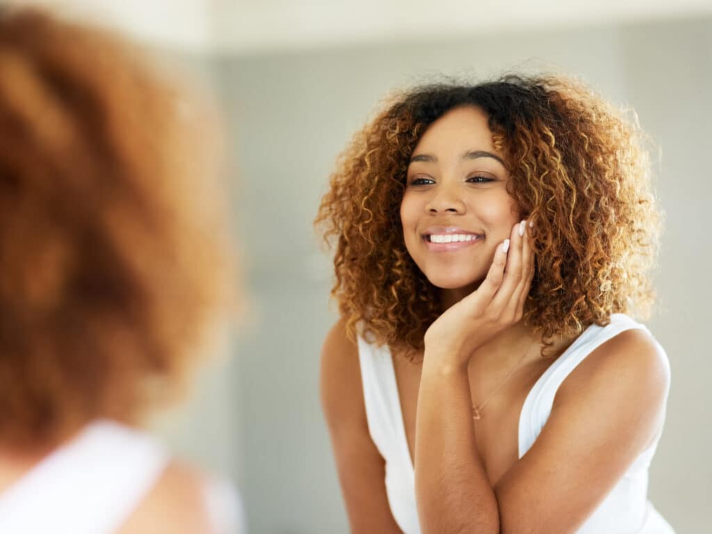 Woman looking at her refreshed face happily in the mirror after getting a glacial skin treatment.