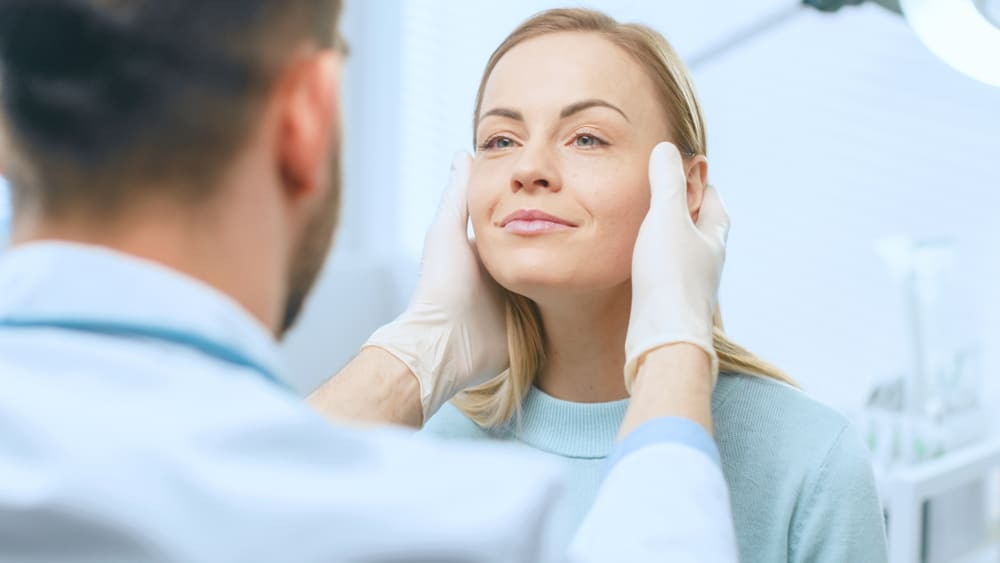 Woman smiling while checking the results of dermal filler injections to address facial volume loss.